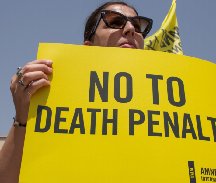 Un militant d'Amnesty portant des lunettes de soleil tient une pancarte sur laquelle on peut lire « Non à la peine de mort ».