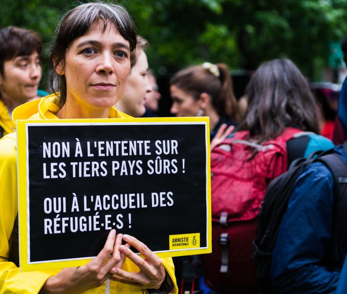 Personne tenant une pancarte "Non à l'entente sur les tiers pays sûrs ! Oui à l'accueil des réfugié·e·s !"