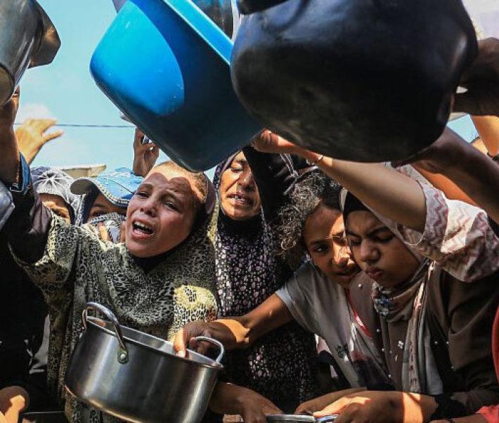 Groupe de femmes et d’enfants brandissant des casseroles et des récipients vides dans une foule, exprimant la faim et le manque de nourriture, scène de crise humanitaire.