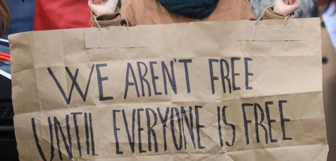 Une personne tenant un écriteau "We aren't free until everyone is free"