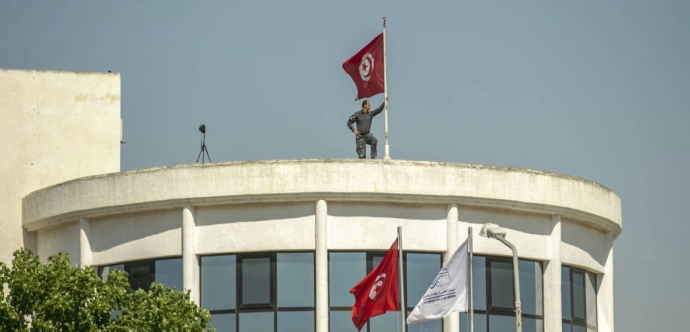 Un militaire tient un drapeau tunisien sur le toit d'un bâtiment 