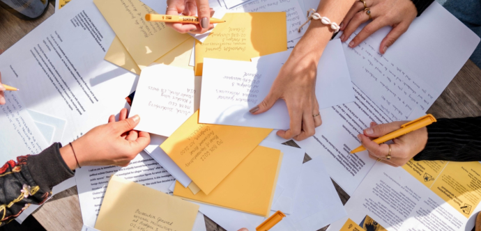 Des lettres sont entassées les unes sur les autres, avec des mains qui tiennent des stylos