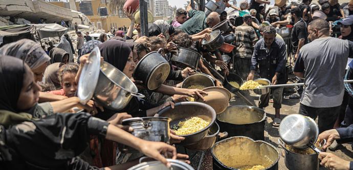 Un groupe de plusieurs personnes qui sont tassés l'un contre l'autre de manière très détresse qui essaient désespérément de remplir leur contenaires de nourritures sachant qu'il yen a trés peu et que c'est une famine