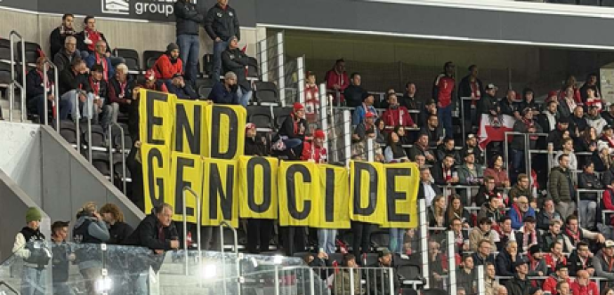 L'image montre des supporters dans les tribunes d'un stade déployant une banderole jaune portant l'inscription « END GENOCIDE » lors d'un match de football de la Ligue des nations de l'UEFA entre l'Autriche et l'Israël à Linz.
