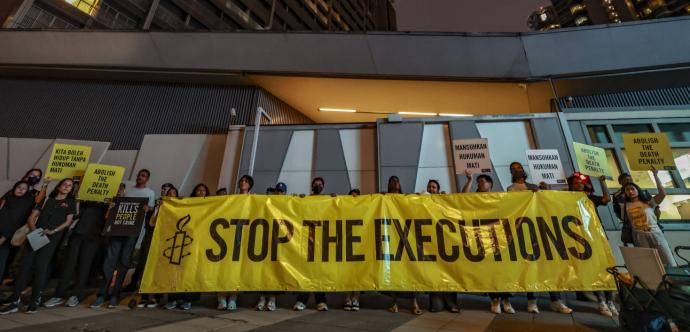 rassemblement de militant·e·s, notamment de l'organisation Amnistie internationale, tenant une grande banderole jaune portant l'inscription « STOP THE EXECUTIONS »