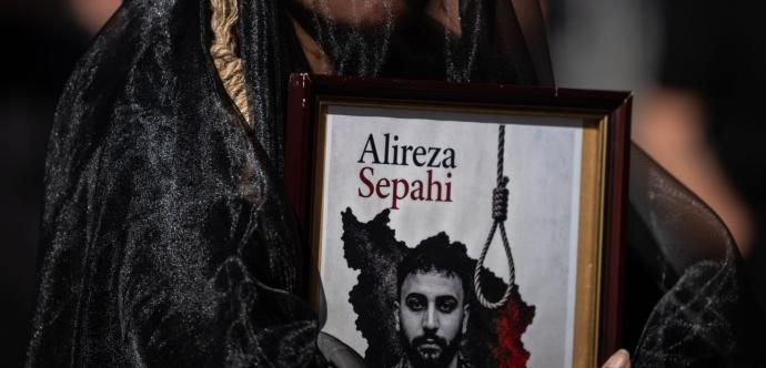 La photo montre un manifestant tenant un portrait de Alireza Sepahi, un manifestant iranien de 25 ans. Celui-ci a été arrêté lors des manifestations anti-régime de janvier 2026 à Ispahan.