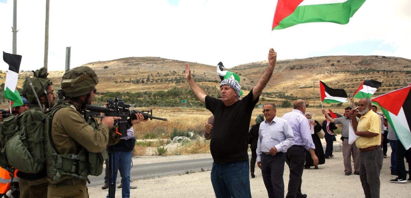 Des palestiniens avec drapeaux devant des militaires armés