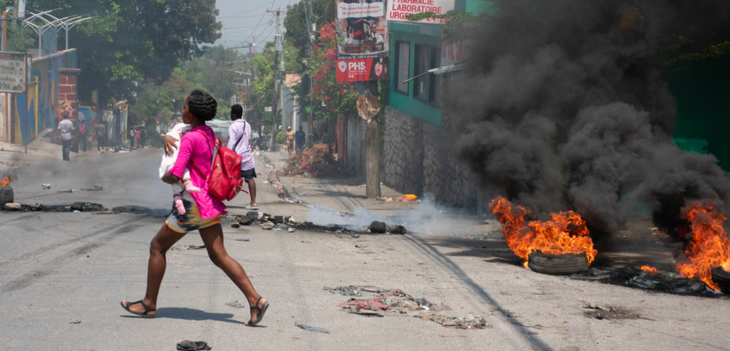 TOPSHOT - Une femme portant un enfant s'enfuit de la zone après que des coups de feu aient été entendus à Port-au-Prince, Haïti, le 20 mars 2024. Les négociations visant à former un conseil de transition pour gouverner Haïti ont progressé le 20 mars, alors que les États-Unis ont transporté par avion de nouveaux citoyens pour les mettre à l'abri de la violence des gangs qui a plongé le pays appauvri dans le chaos.