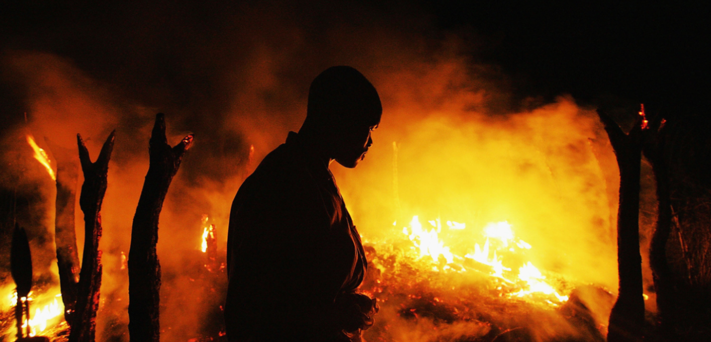 Un homme devant une forêt en feu, la nuit.