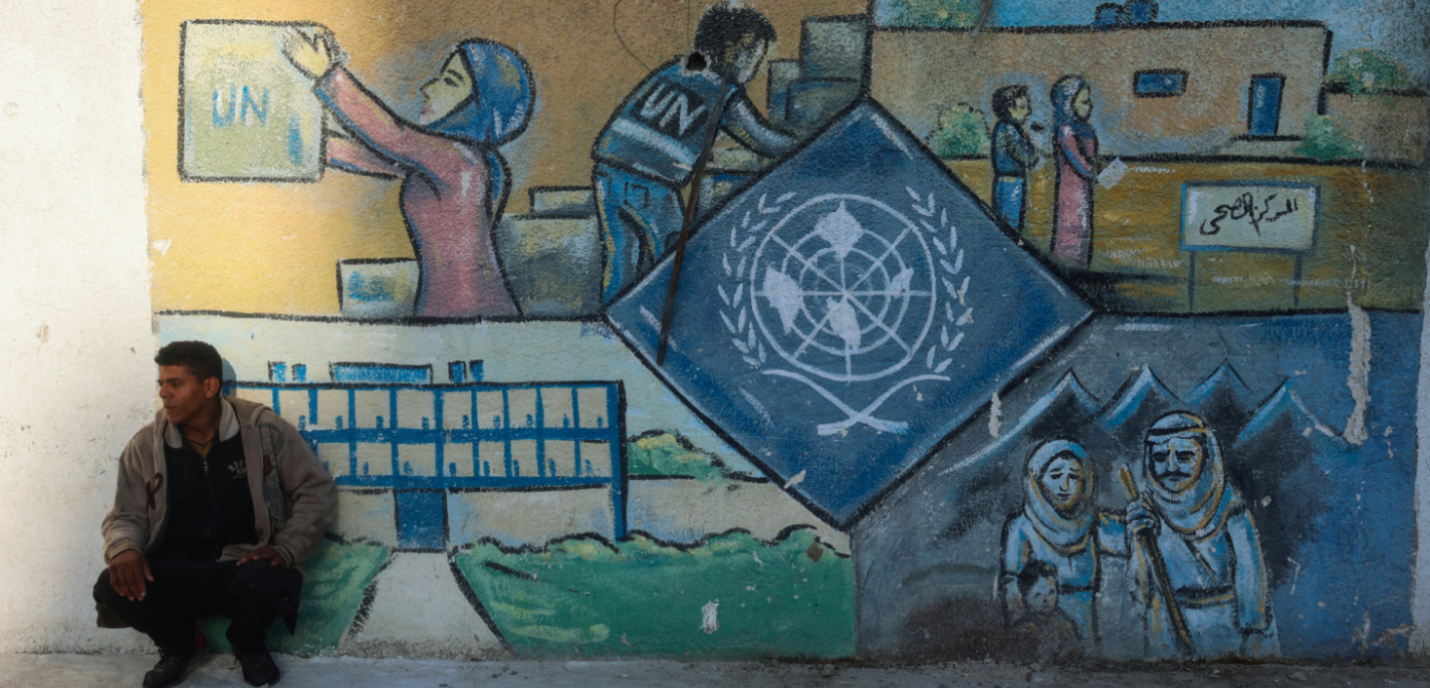 Un homme accroupi devant une peinture murale représentant le logo des nations unies