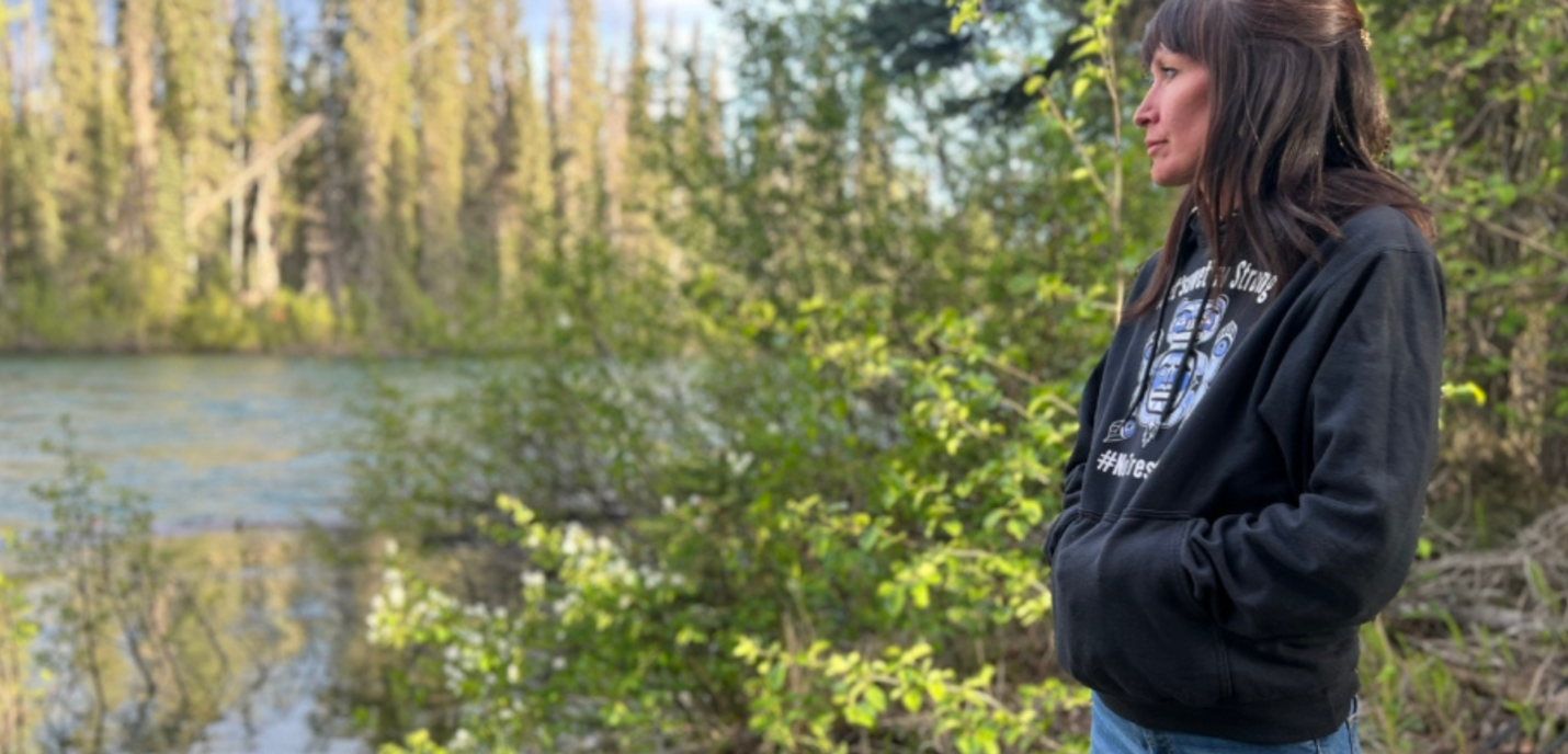 Une femme portant un sweat à capuche noir et un jean bleu regarde vers une rivière.