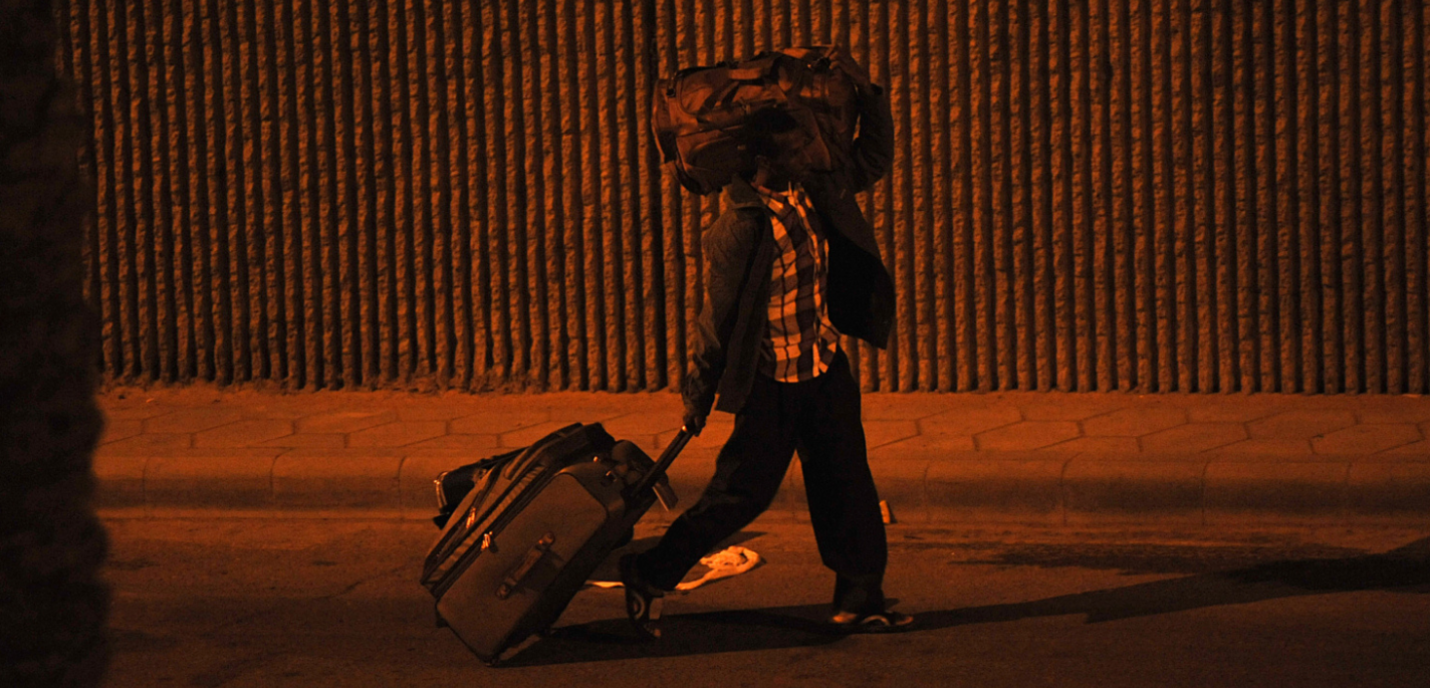 Une personne marche dans la rue avec une valide et un sac de transport sur l'épaule gauche