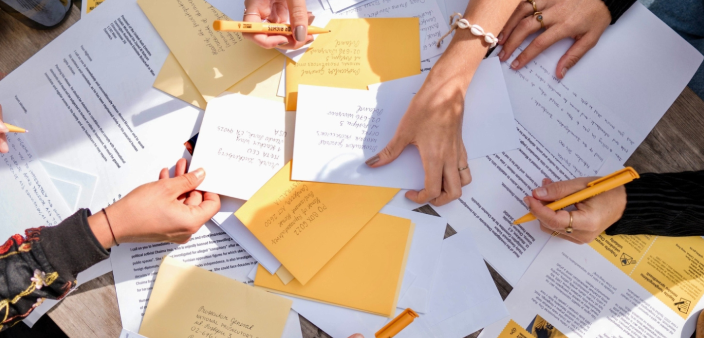 Des lettres sont entassées les unes sur les autres, avec des mains qui tiennent des stylos