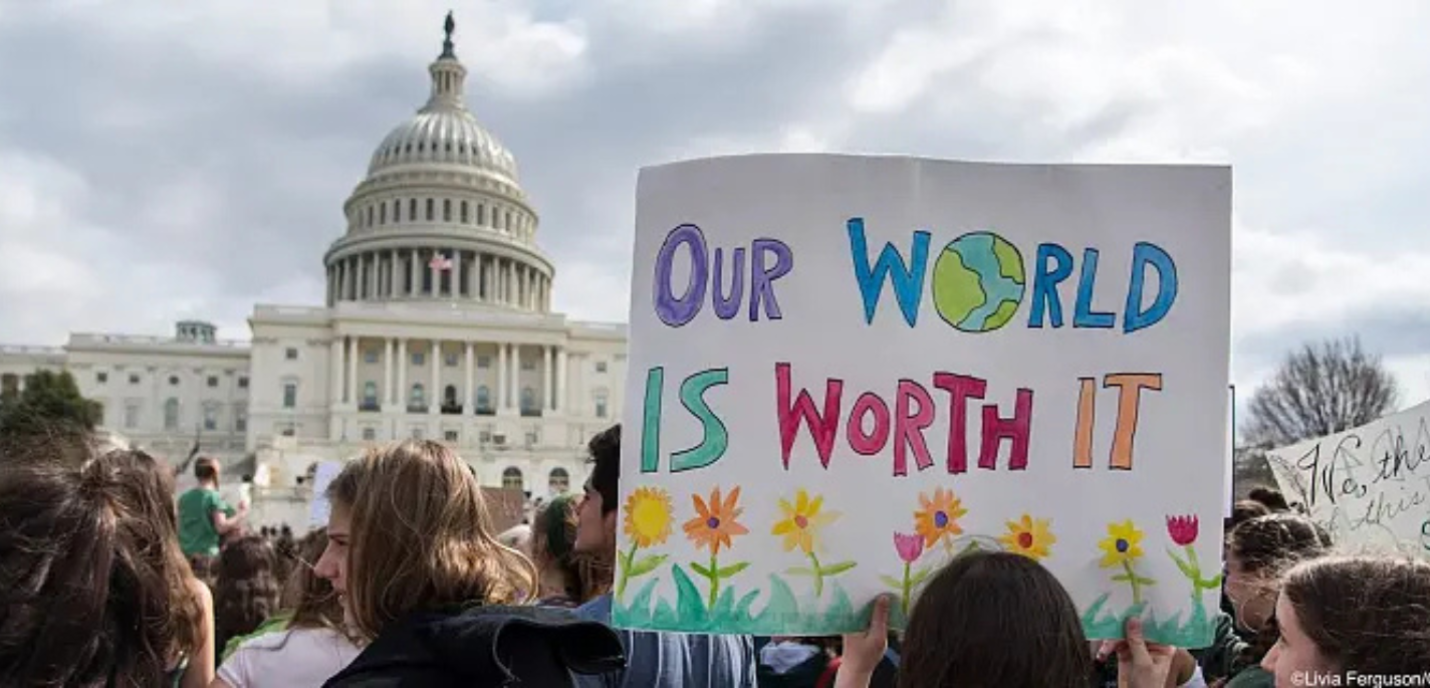 Une manifestation devant le capitole aux États-Unis, avec un premier plan une pancarte "Our World is worth it"