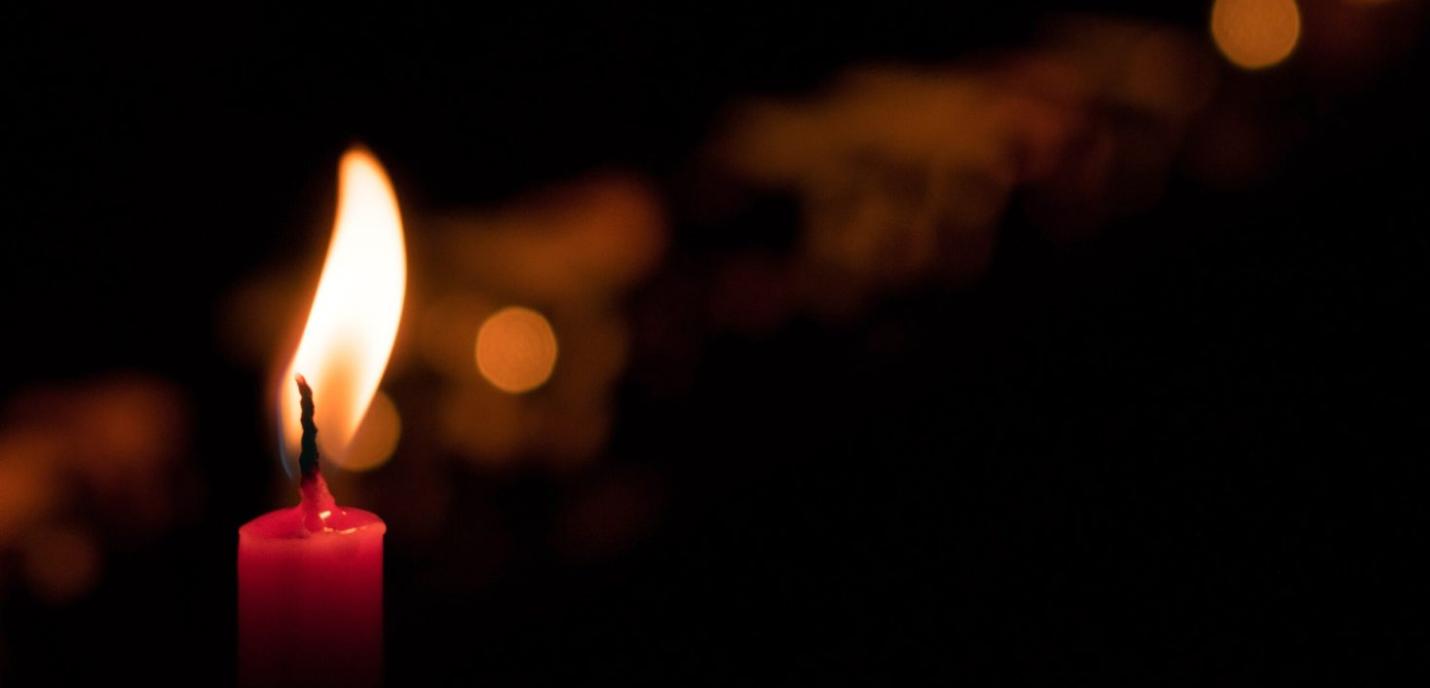 Une bougie rouge allumée dans l’obscurité, sa flamme éclaire légèrement l’arrière-plan sombre et flou.