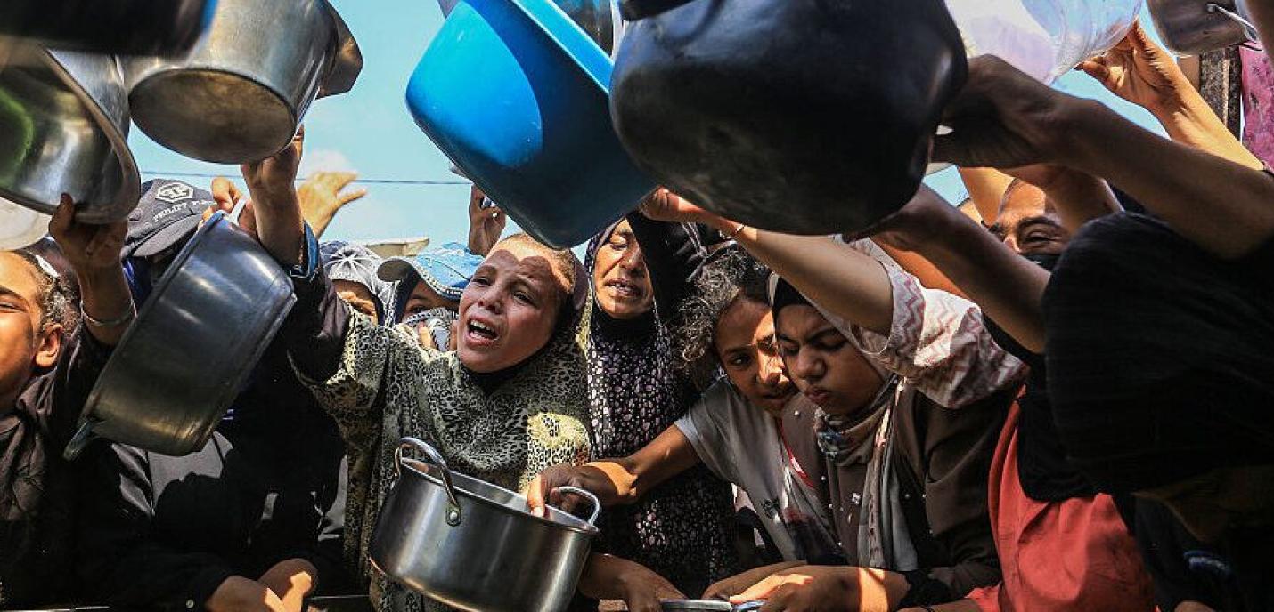 Groupe de femmes et d’enfants brandissant des casseroles et des récipients vides dans une foule, exprimant la faim et le manque de nourriture, scène de crise humanitaire.
