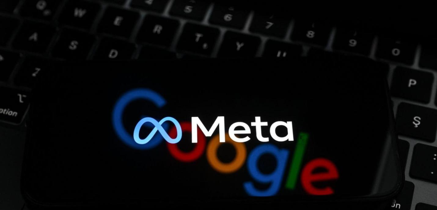 Un gros plan d’un écran affichant les logos de Meta (au premier plan, en blanc avec l’icône en forme d’infini bleu) et de Google (en arrière-plan, flou, avec ses lettres colorées), le tout posé sur un clavier d’ordinateur noir.