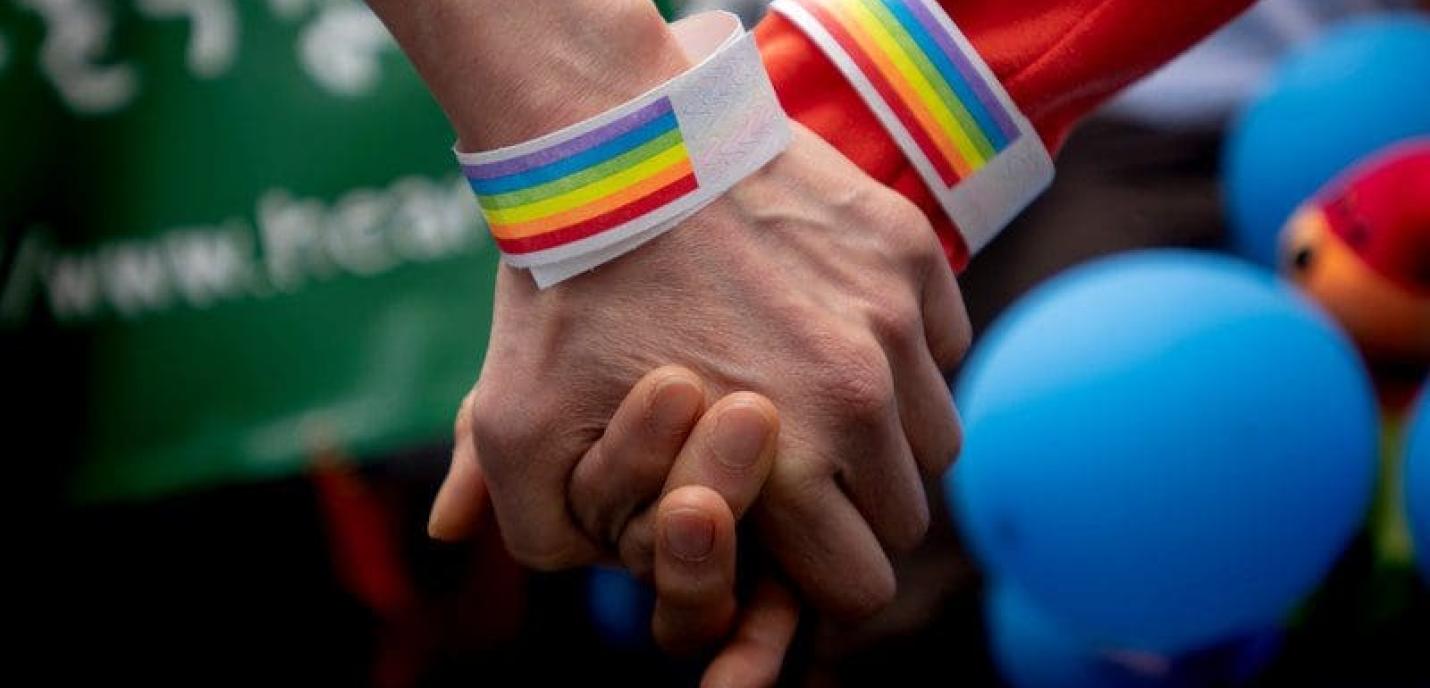 deux mains qui se tiennent et qui mettent des bracelets arc-en-ciel LGBTQ