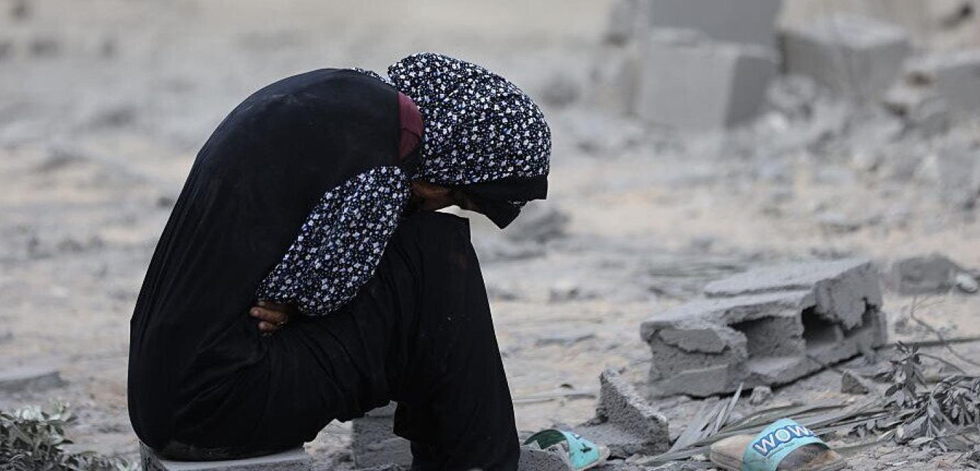 Jeune palestinienne assise dans des débris, se tenant la tête.