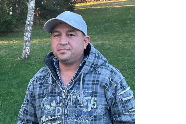 Photo portrait de Miguel, un travailleur d'Amérique centrale. Il se trouve dans un jardin et porte une casquette et un sweatshirt.