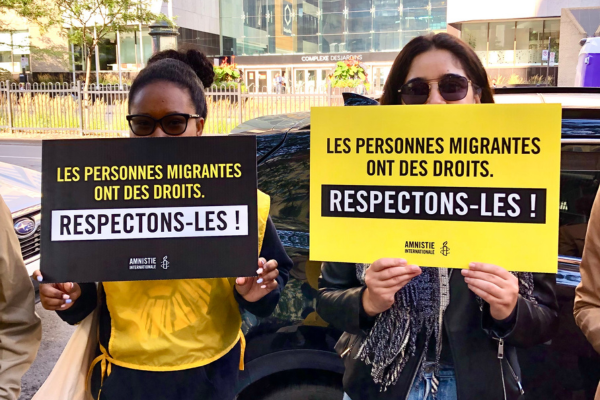 Deux militantes d'Amnistie internationale tiennent des pancartes indiquant "Les personnes migrantes ont des droits. Respectons-les"