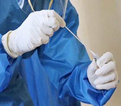 Une personne vêtue d'une blouse médicale bleue et de gants tient un échantillon dans ses mains.