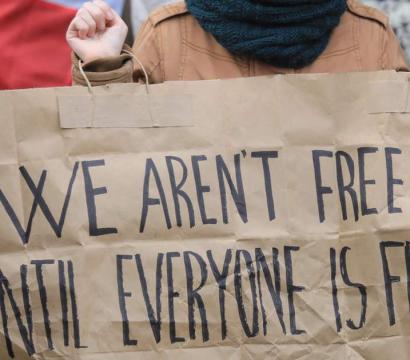 Une personne tenant un écriteau "We aren't free until everyone is free"