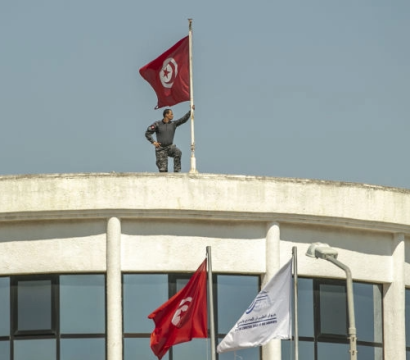 Un militaire tient un drapeau tunisien sur le toit d'un bâtiment 