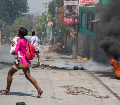 TOPSHOT - Une femme portant un enfant s'enfuit de la zone après que des coups de feu aient été entendus à Port-au-Prince, Haïti, le 20 mars 2024. Les négociations visant à former un conseil de transition pour gouverner Haïti ont progressé le 20 mars, alors que les États-Unis ont transporté par avion de nouveaux citoyens pour les mettre à l'abri de la violence des gangs qui a plongé le pays appauvri dans le chaos.