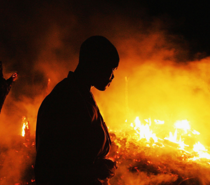 Un homme devant une forêt en feu, la nuit.