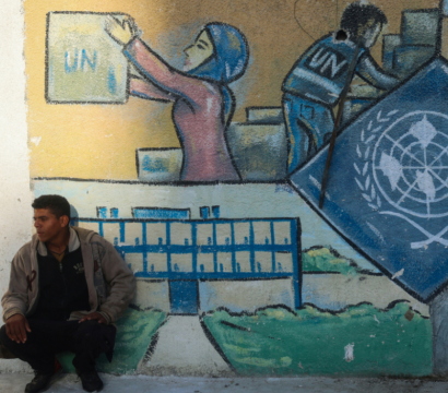 Un homme accroupi devant une peinture murale représentant le logo des nations unies