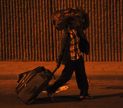 Une personne marche dans la rue avec une valide et un sac de transport sur l'épaule gauche