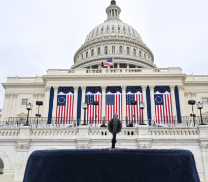 Photo du capitole aux États-Unis, avec un pupitre et un micro en premier plan et des drapeaux du pays en second plan.