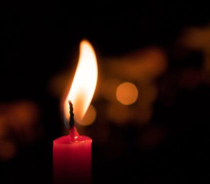 Une bougie rouge allumée dans l’obscurité, sa flamme éclaire légèrement l’arrière-plan sombre et flou.