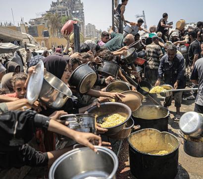 Un groupe de plusieurs personnes qui sont tassés l'un contre l'autre de manière très détresse qui essaient désespérément de remplir leur contenaires de nourritures sachant qu'il yen a trés peu et que c'est une famine