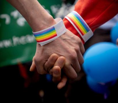 deux mains qui se tiennent et qui mettent des bracelets arc-en-ciel LGBTQ