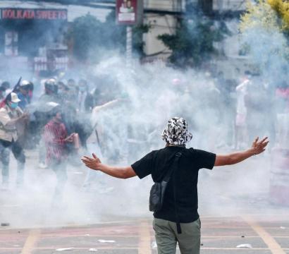 Homme de dos avec les bras ouverts vers le ciel et du gaz autour de lui dans la rue en plein jour 