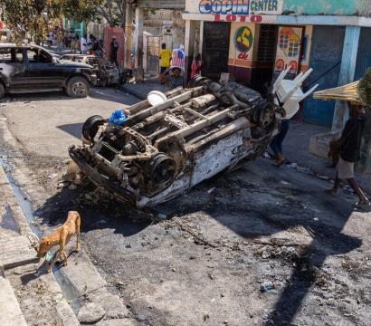 Une carcasse de voiture calcinée, retournée en travers de la chaussée, témoigne d’une scène de violence.