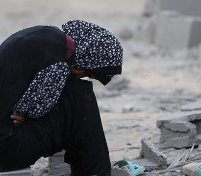 Jeune palestinienne assise dans des débris, se tenant la tête.