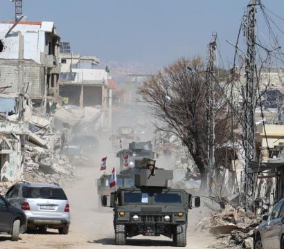 Une ville détruite par des bombes est en arrière plan. On voit des chars militaires sur une route.