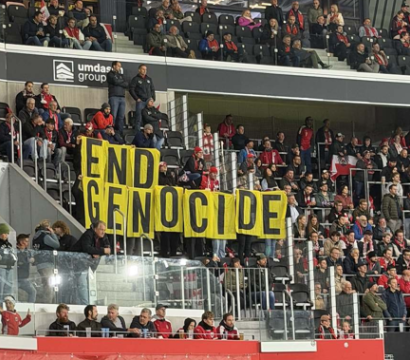 L'image montre des supporters dans les tribunes d'un stade déployant une banderole jaune portant l'inscription « END GENOCIDE » lors d'un match de football de la Ligue des nations de l'UEFA entre l'Autriche et l'Israël à Linz.