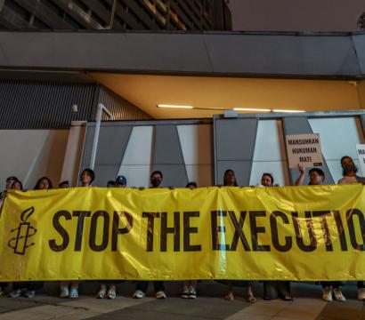 rassemblement de militant·e·s, notamment de l'organisation Amnistie internationale, tenant une grande banderole jaune portant l'inscription « STOP THE EXECUTIONS »